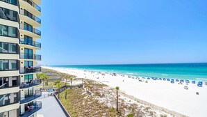 A beachfront hotel with balconies, a sandy beach, and a clear blue sky. - Sunbird 508e (Panama City Beach)
