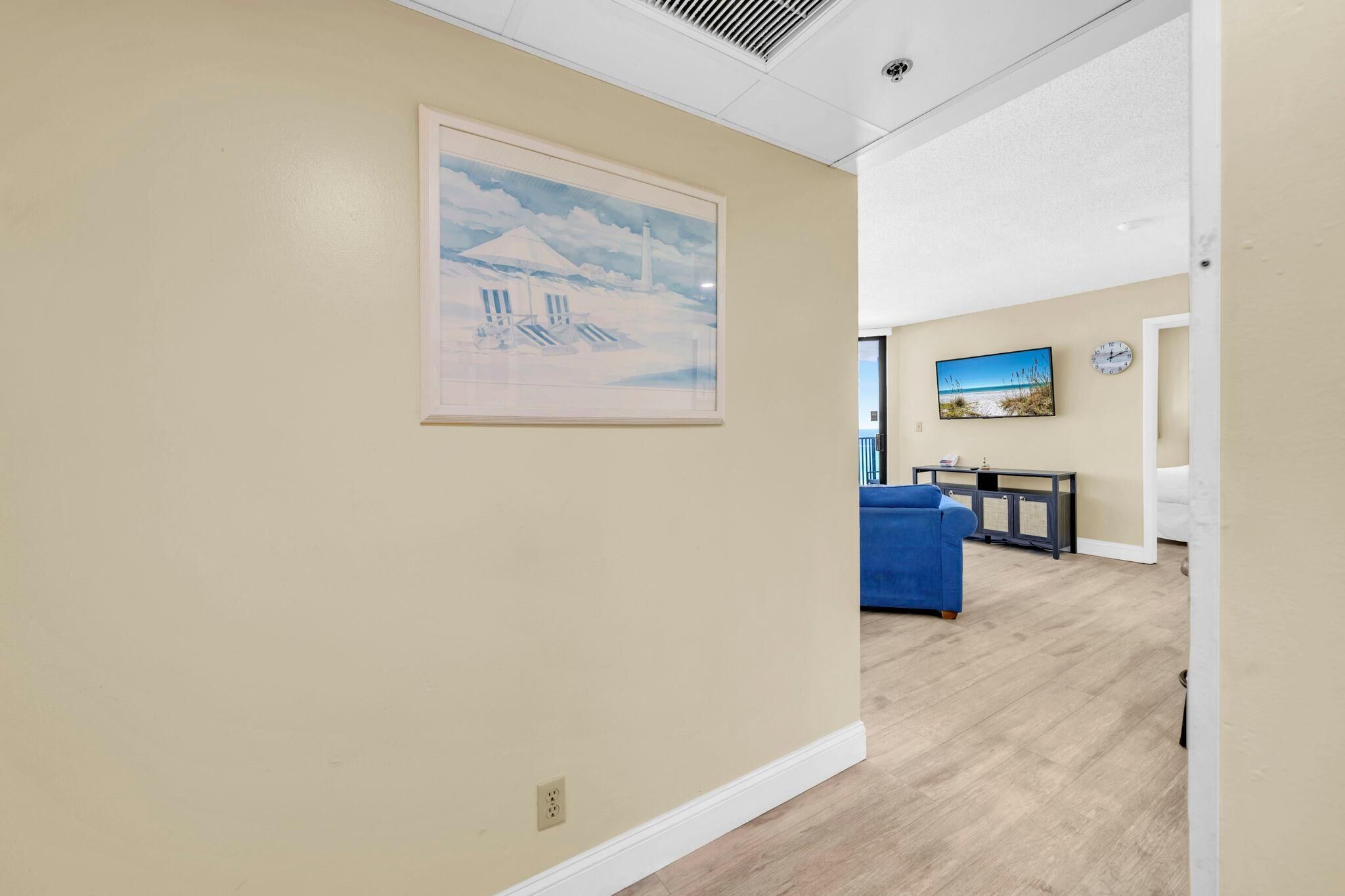 A hallway with a framed artwork, a blue sofa, a small table, and a television.
