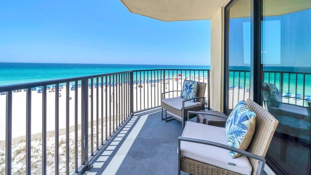 A balcony with wicker furniture, a view of the beach, and a clear sky. - Sunbird 508e (Panama City Beach)