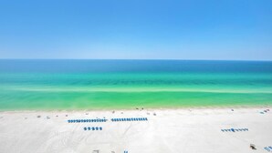 Een strand met helder turquoise water, wit zand en enkele parasols en ligstoelen.