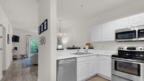 A modern kitchen with white cabinetry, stainless steel appliances, and a built-in dishwasher. - Heron's Watch Way 4104- Coach's Sand Dollar (Santa Rosa Beach)