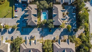 An aerial view of a residential area with a central swimming pool surrounded by houses, a parking lot, and trees. - Heron's Watch Way 4104- Coach's Sand Dollar (Santa Rosa Beach)
