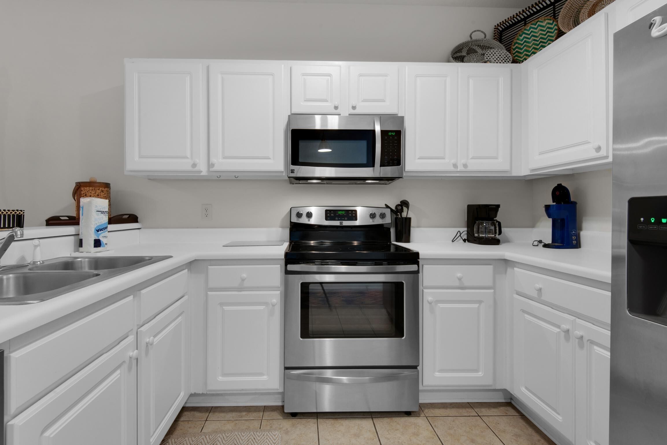 A kitchen with white cabinets, a stainless steel microwave, a stove, and a coffee maker.