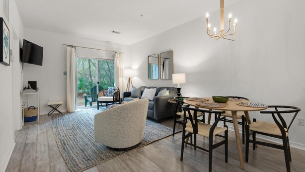 A modern living room with a dining area, a sofa, a TV, and a view of the outdoors. - Heron's Watch Way 4104- Coach's Sand Dollar (Santa Rosa Beach)