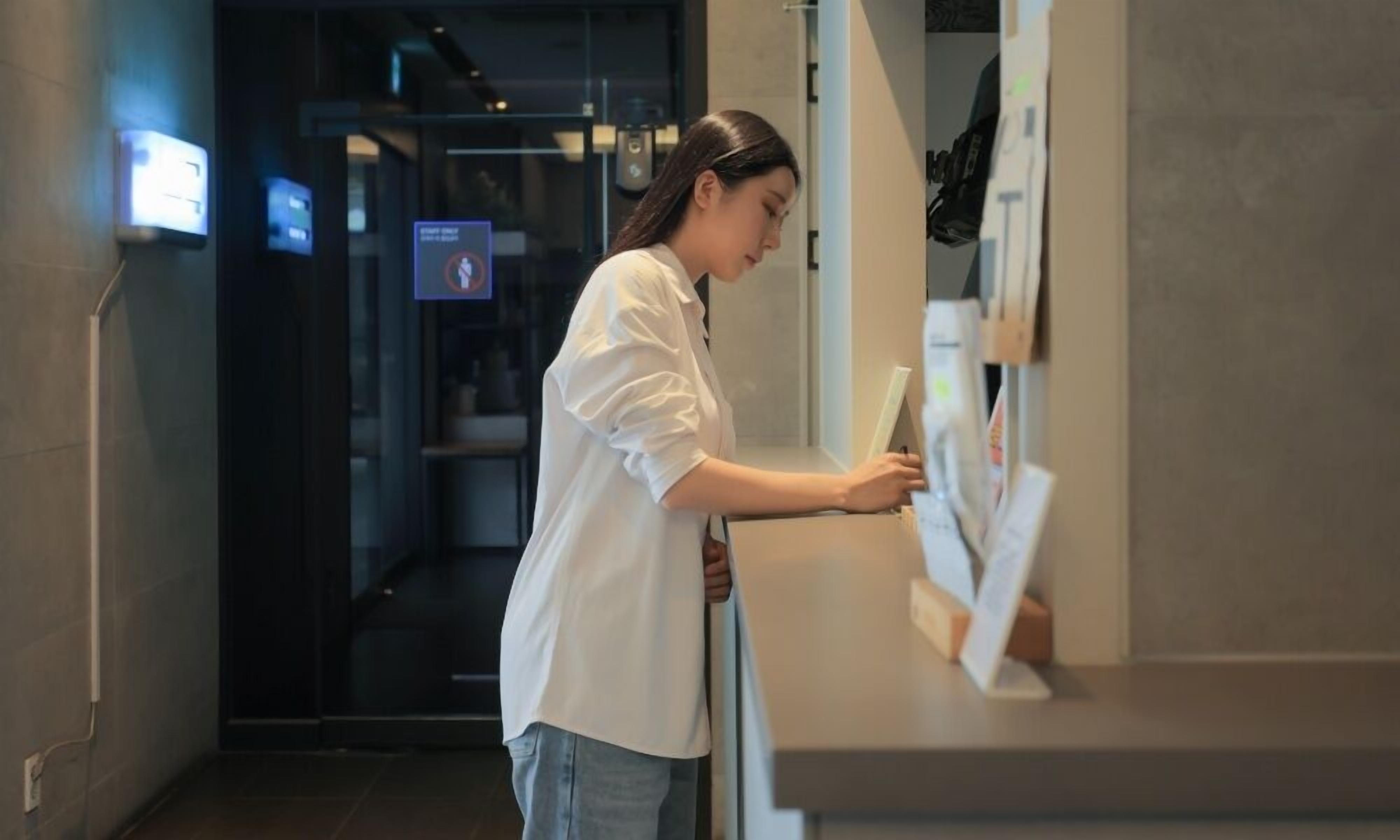 A person at a reception desk in a modern building with glass doors and a digital display.