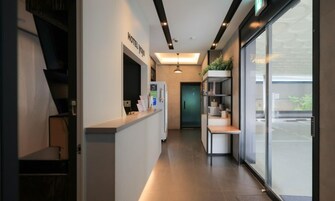 Zona de recepción de hotel con diseño moderno, una mesa de recepción, una puerta de cristal que da al vestíbulo y una escalera visible.