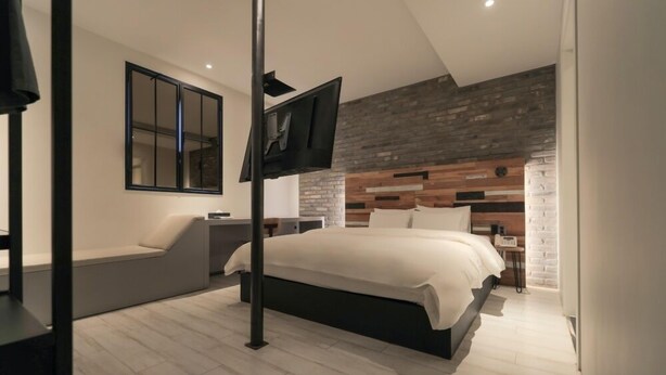 Ein modernes Schlafzimmer mit einem großen Bett, einem an einem Pfosten befestigten Fernseher, einem hölzernen Kopfteil und einer Bank am Fenster.