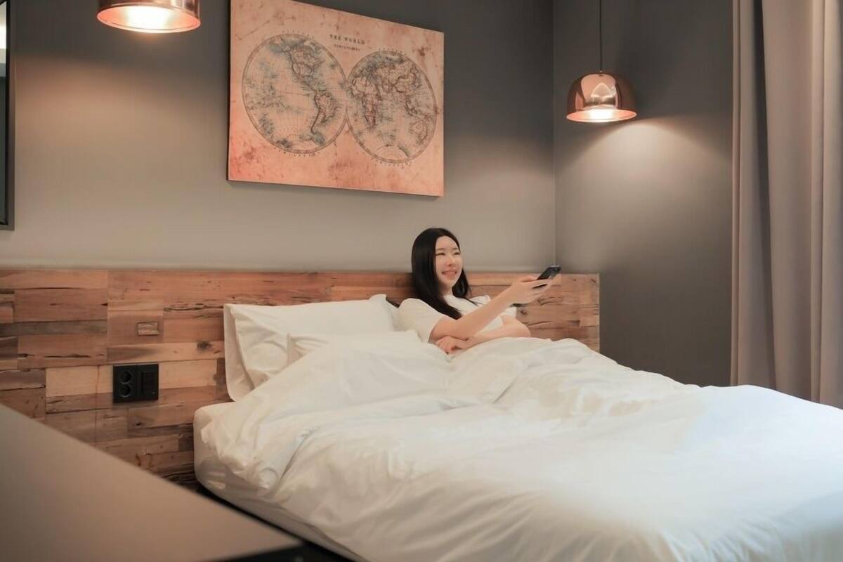 A bed with white bedding, a wooden headboard, and a world map on the wall.