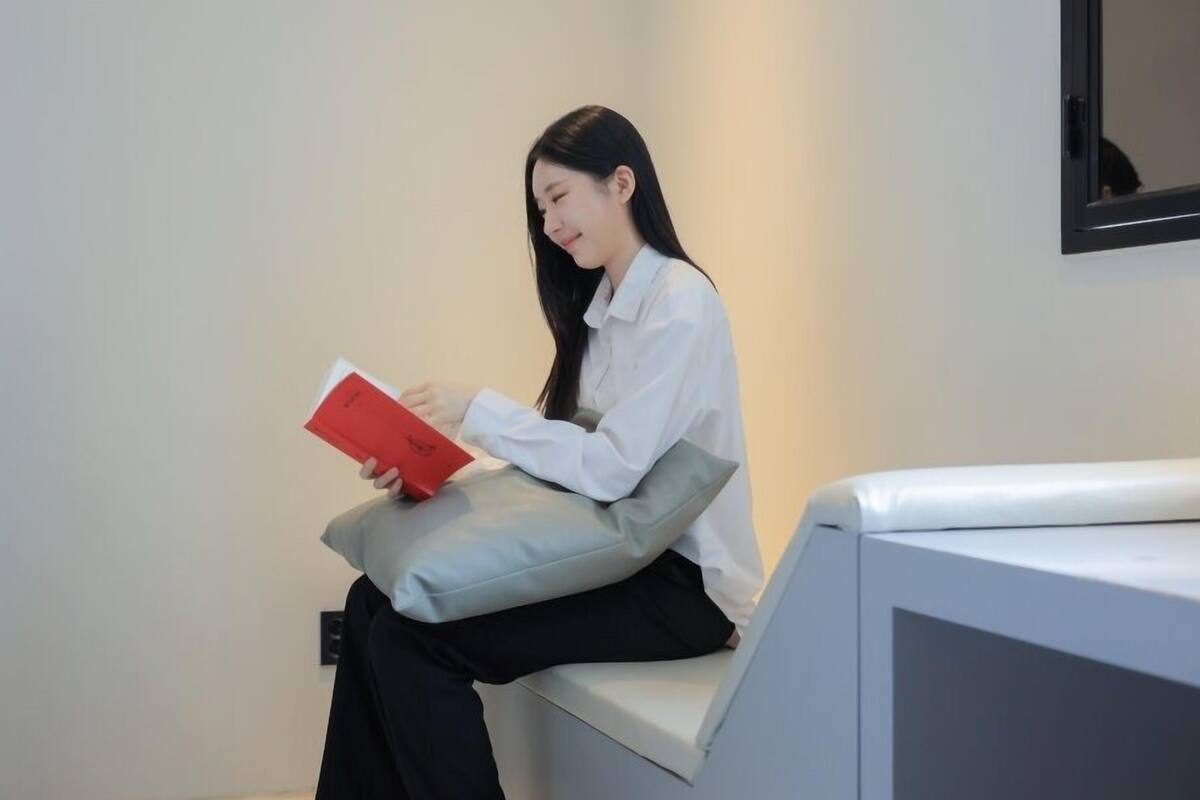A person sitting on a bench reading a red book.