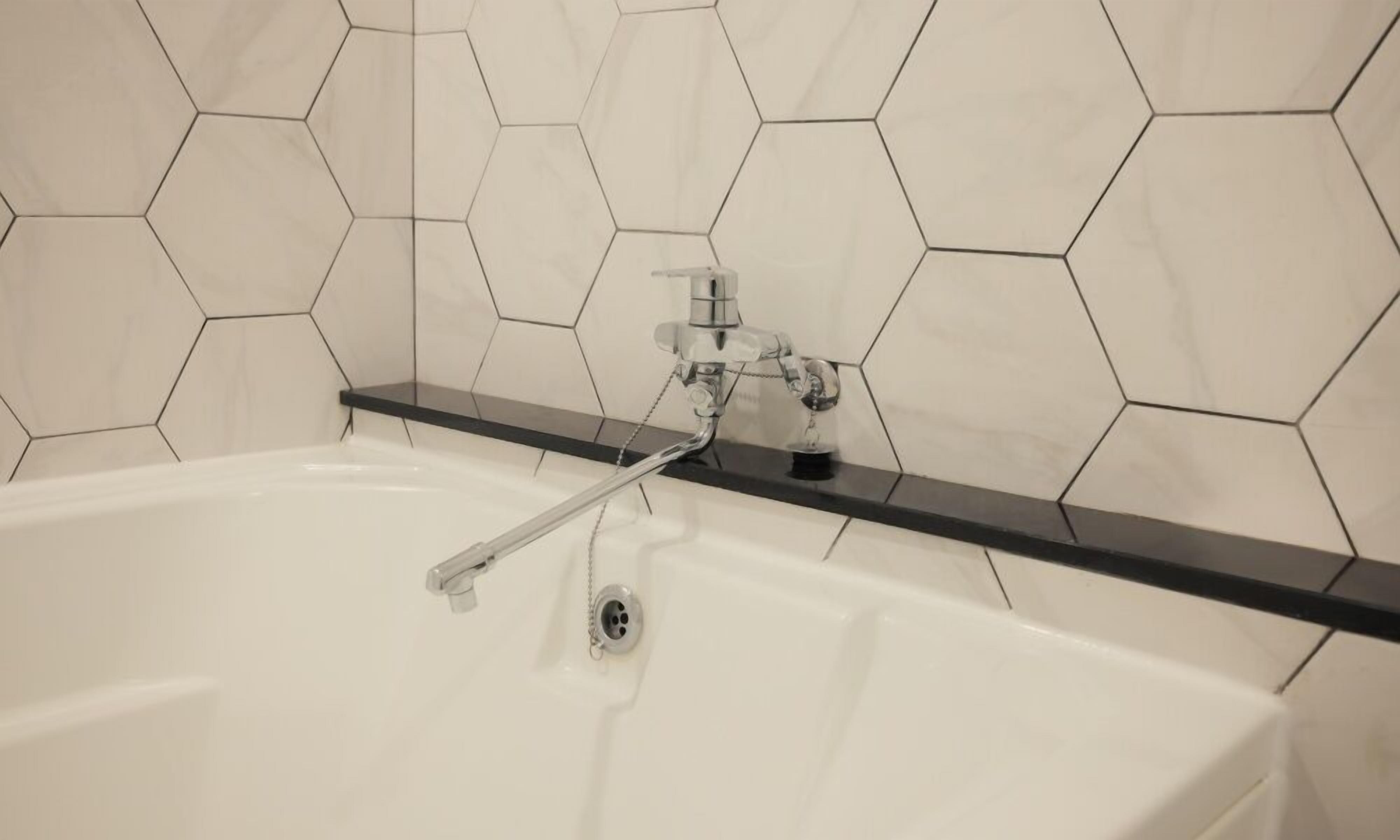 Un baño con una bañera blanca, un mostrador negro y baldosas blancas hexagonales en la pared.