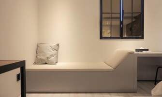 Una habitación minimalista con un banco empotrado, una mesita pequeña y un ventanal.