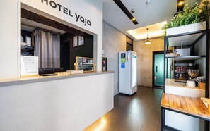 A hotel reception area with a counter, a refrigerator, and a plant.
