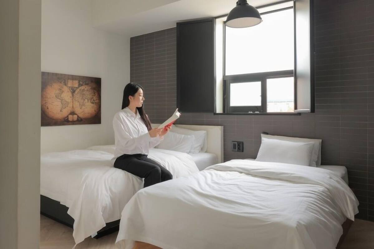 A modern hotel room with two single beds, a large window with a view, and a globe artwork on the wall.