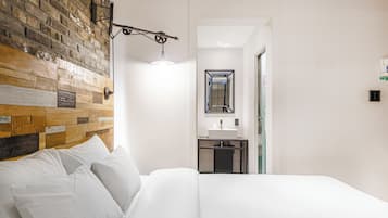 Habitación de hotel con pared de ladrillo, cama con ropa de cama blanca, lámpara colgante y vista al baño.
