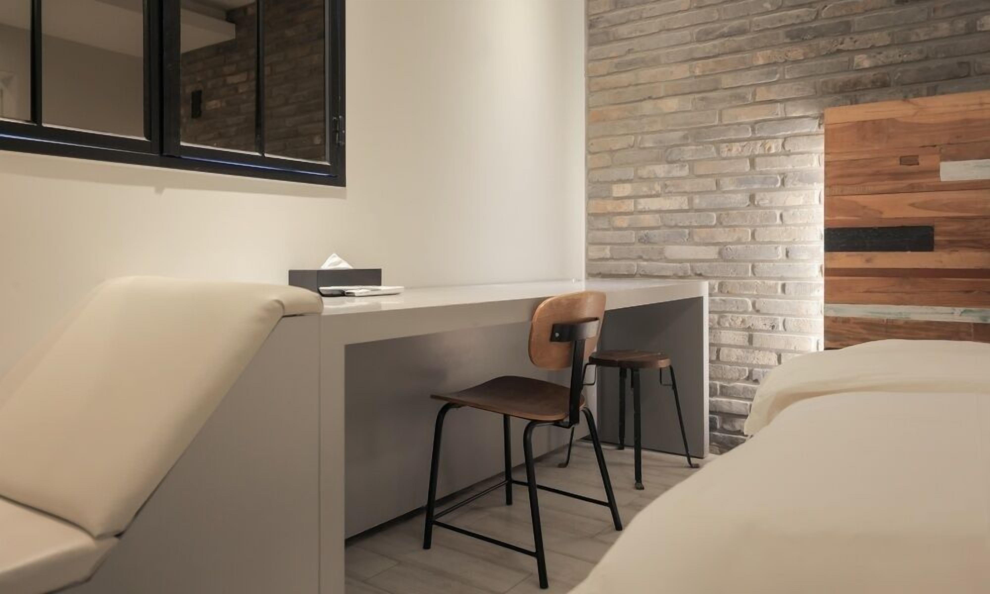Une chambre d’hôtel moderne au design minimaliste, comprenant un bureau avec une chaise, un grand miroir et deux lits.