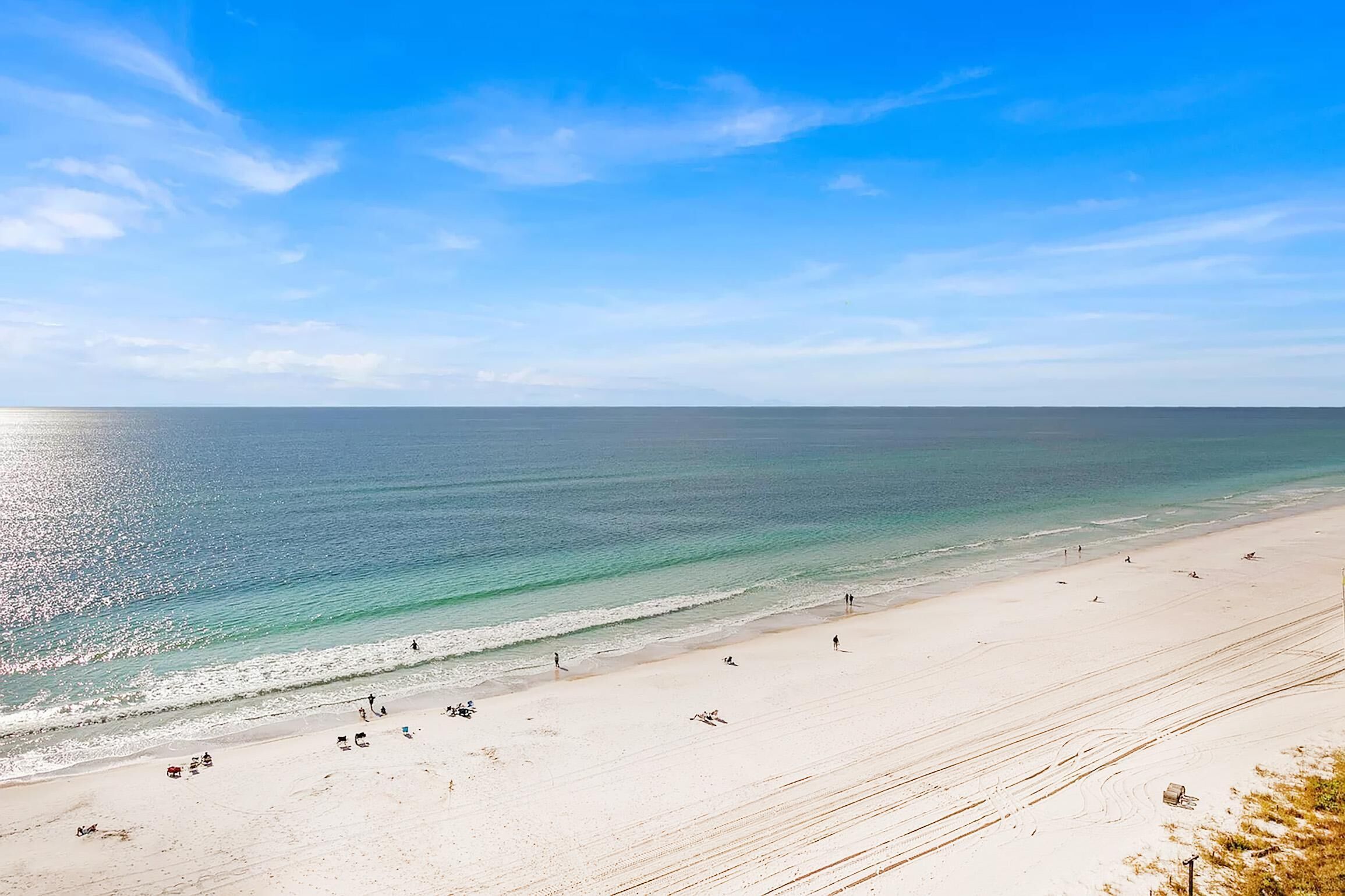 A wide beach with clear blue water and a few people.