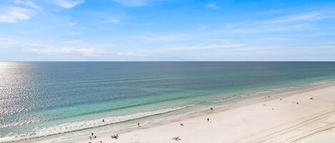 A wide beach with clear blue water and a few people.