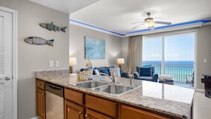 A kitchen with granite countertops, a double sink, wooden cabinets, and a dining area with a view of the ocean. - Splash 603e (Panama City Beach)