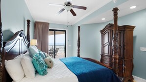 Une chambre avec un grand lit, un ventilateur de plafond, une armoire en bois et une vue sur le balcon.