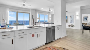 A modern kitchen with white cabinetry, a dishwasher, and a view of the ocean. - Hidden Dunes 1802 (Panama City Beach)