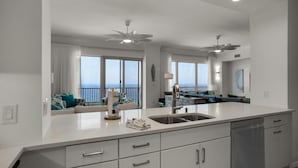 A modern kitchen with a large island, a dining area with a view, and a ceiling fan. - Hidden Dunes 1802 (Panama City Beach)