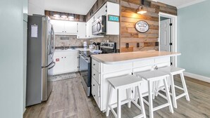 A modern kitchen with white cabinets, a wooden accent wall, a built-in microwave, and a bar area with stools. - The Summit 924 (Panama City Beach)