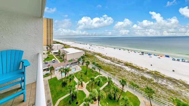 A balcony with a blue chair overlooking a beach with a hotel building in the background. - The Summit 924 (Panama City Beach)