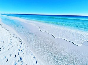 Una playa con agua azul cristalina y un muelle a lo lejos.