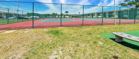 A tennis court with a green fence, a red track, and a green field area.