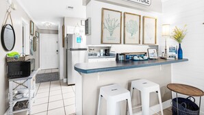 A modern kitchen with a blue countertop, white stools, and a sign that reads "OUR HAPPY PLACE". - Gulf Highlands 116h (Panama City Beach)