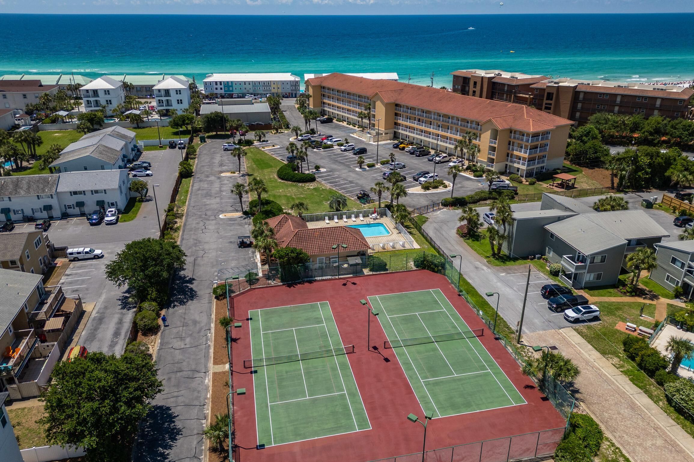 A coastal hotel with two tennis courts, a swimming pool, and a parking lot.