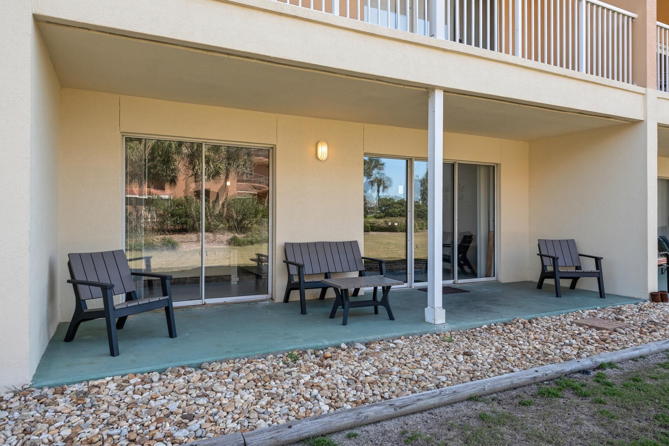 A covered outdoor area with three Adirondack chairs, a concrete floor, and a gravel border.