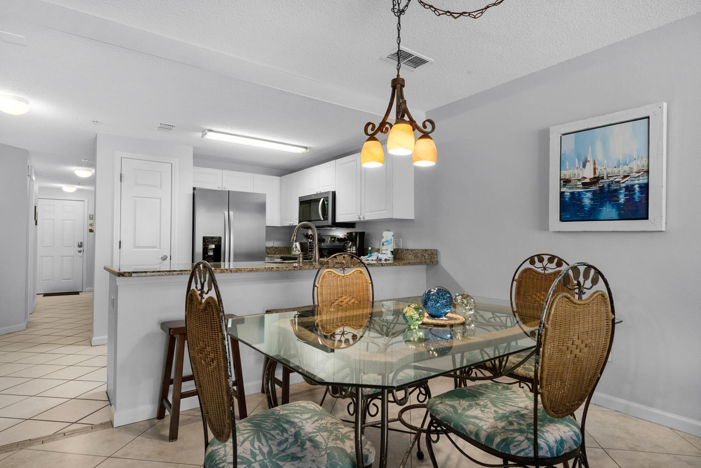 A modern kitchen with white cabinets, a stainless steel refrigerator, and a dining area with a glass table and wicker chairs.