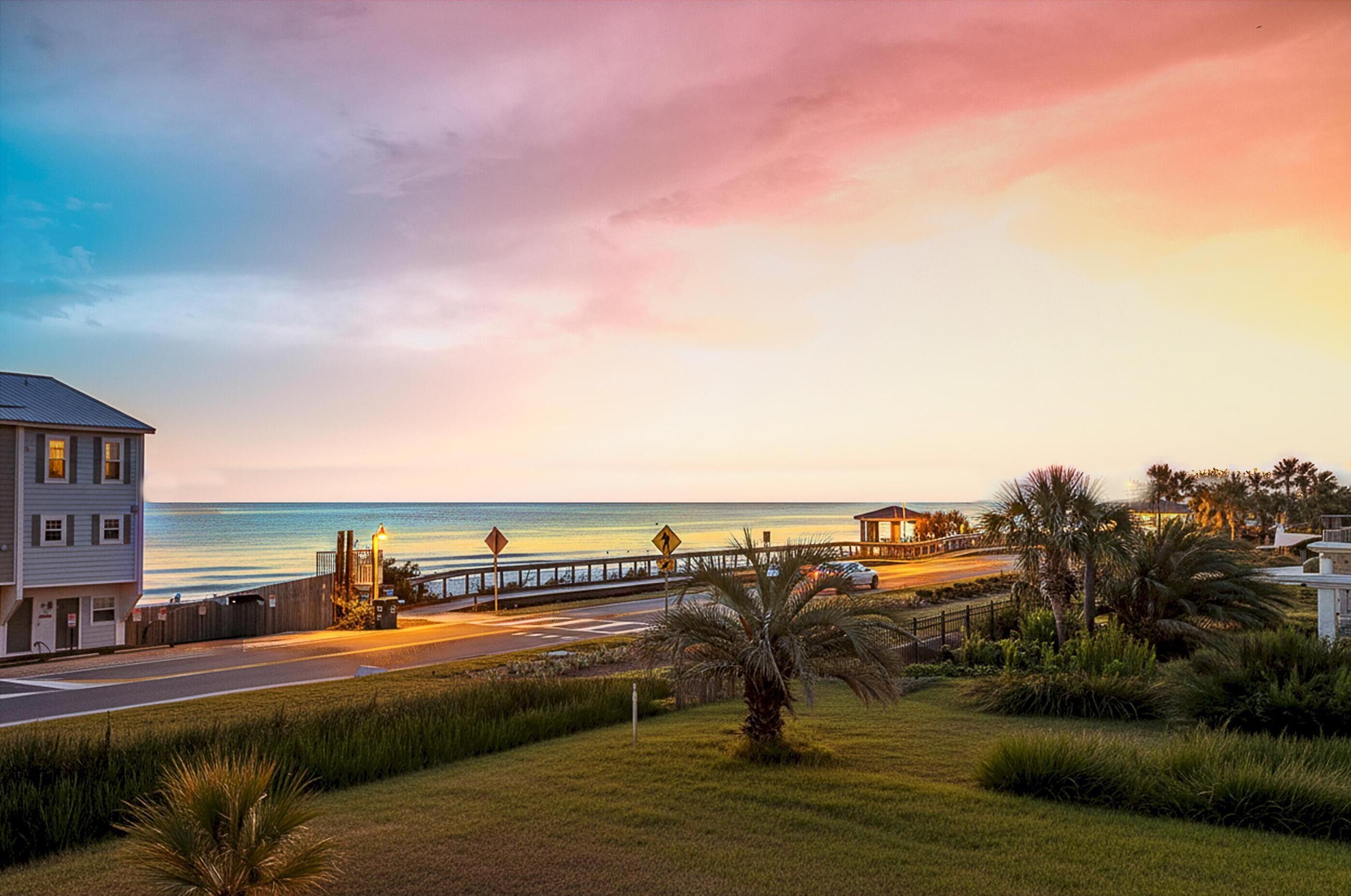 A coastal road with a pedestrian crossing, a beach, and a building with a porch.