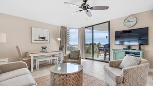 A spacious living room with a ceiling fan, a dining area with a table and chairs, a sofa, a coffee table, and a TV mounted on the wall. - Mainsail 213 (Miramar Beach)