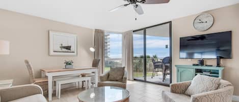 A spacious living room with a ceiling fan, a dining area with a table and chairs, a sofa, a coffee table, and a TV mounted on the wall.