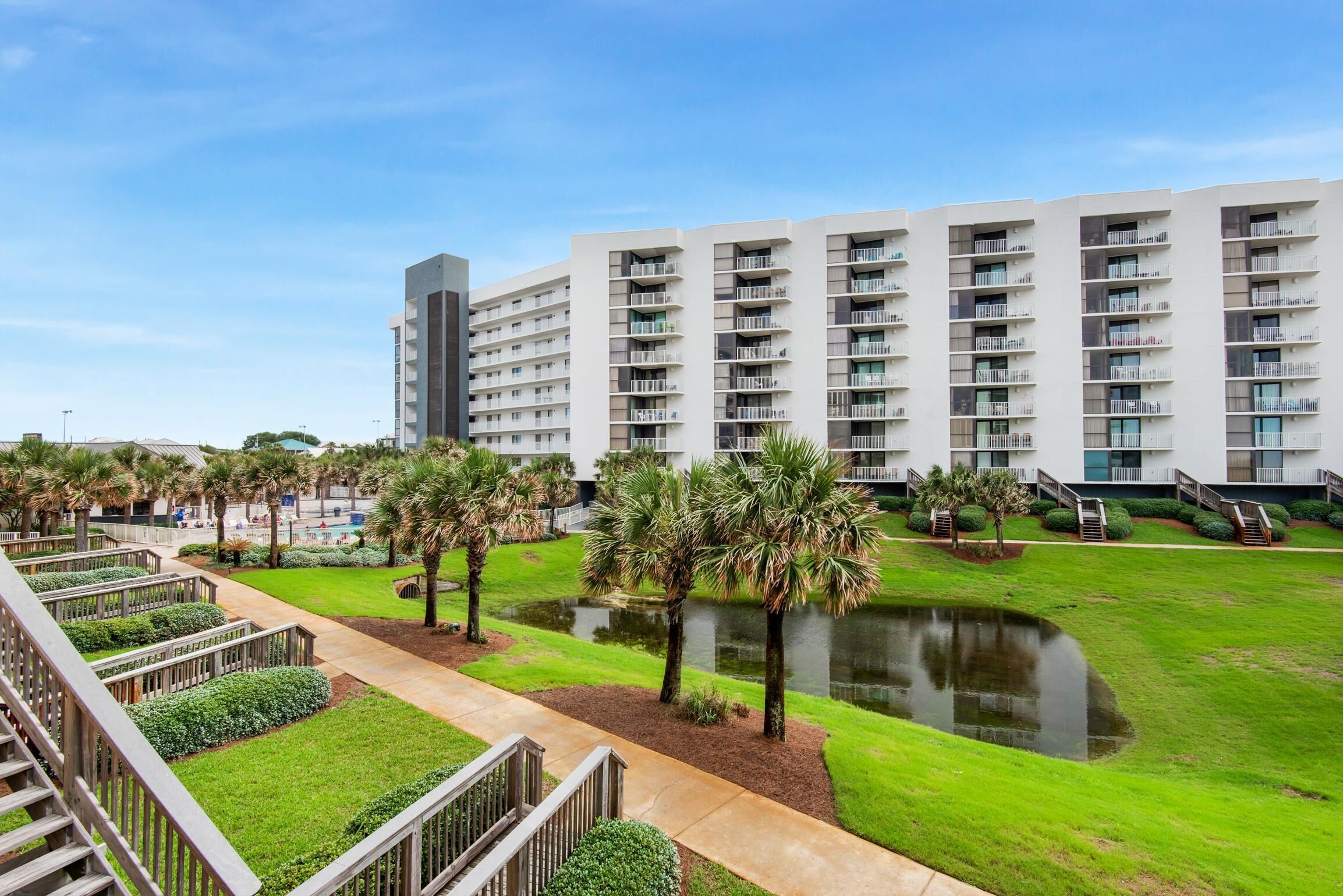 A modern hotel with multiple floors, a central courtyard with a pond, and a well-maintained lawn.
