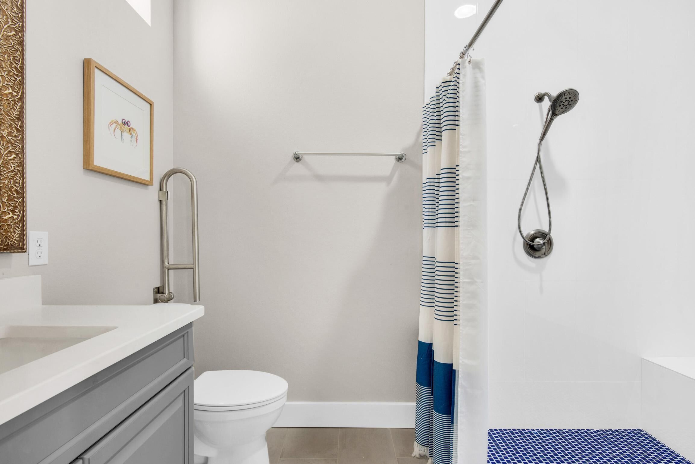 Un baño con inodoro, ducha con cortina a rayas, toallero y un cuadro en la pared.