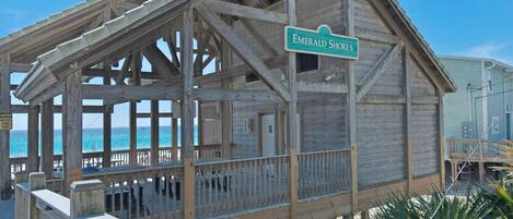 A wooden beach house with a covered porch and a sign reading "Emerald Shores".