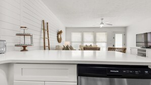 Egy modern konyha fehér szekrényekkel, beépített mosogatógéppel és mennyezeti ventilátorral.