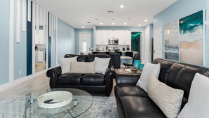 A modern living room with a black leather sofa, a glass coffee table, and a kitchen in the background. - Townhome with Screened Patio, Games Area & Close to Pool (Kissimmee)