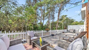 Une terrasse extérieure avec des meubles en osier, une clôture blanche en bois et une vue sur les arbres.