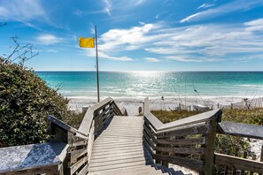 A wooden staircase leading to a beach with a flag on a pole. - Chasing Sunsets (Santa Rosa Beach)
