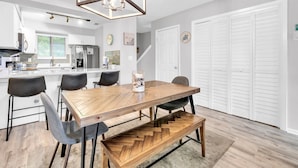 A modern kitchen with white cabinets, a central island, and a dining area with a wooden table and chairs. - Portside R4 (Panama City Beach)