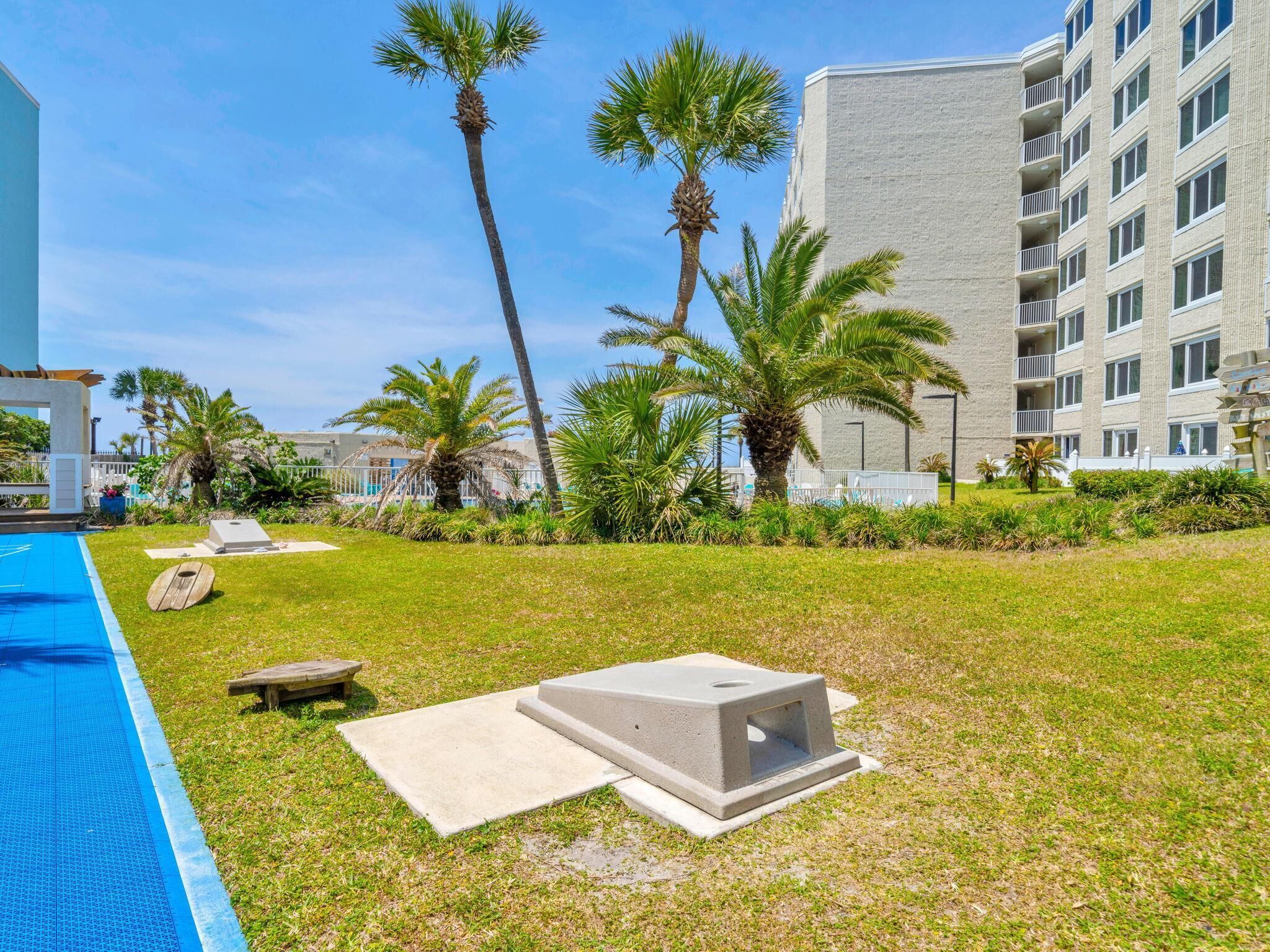 Un área de piscina con una piscina azul cristalina, sillas de descanso, palmeras y un edificio con varios balcones.