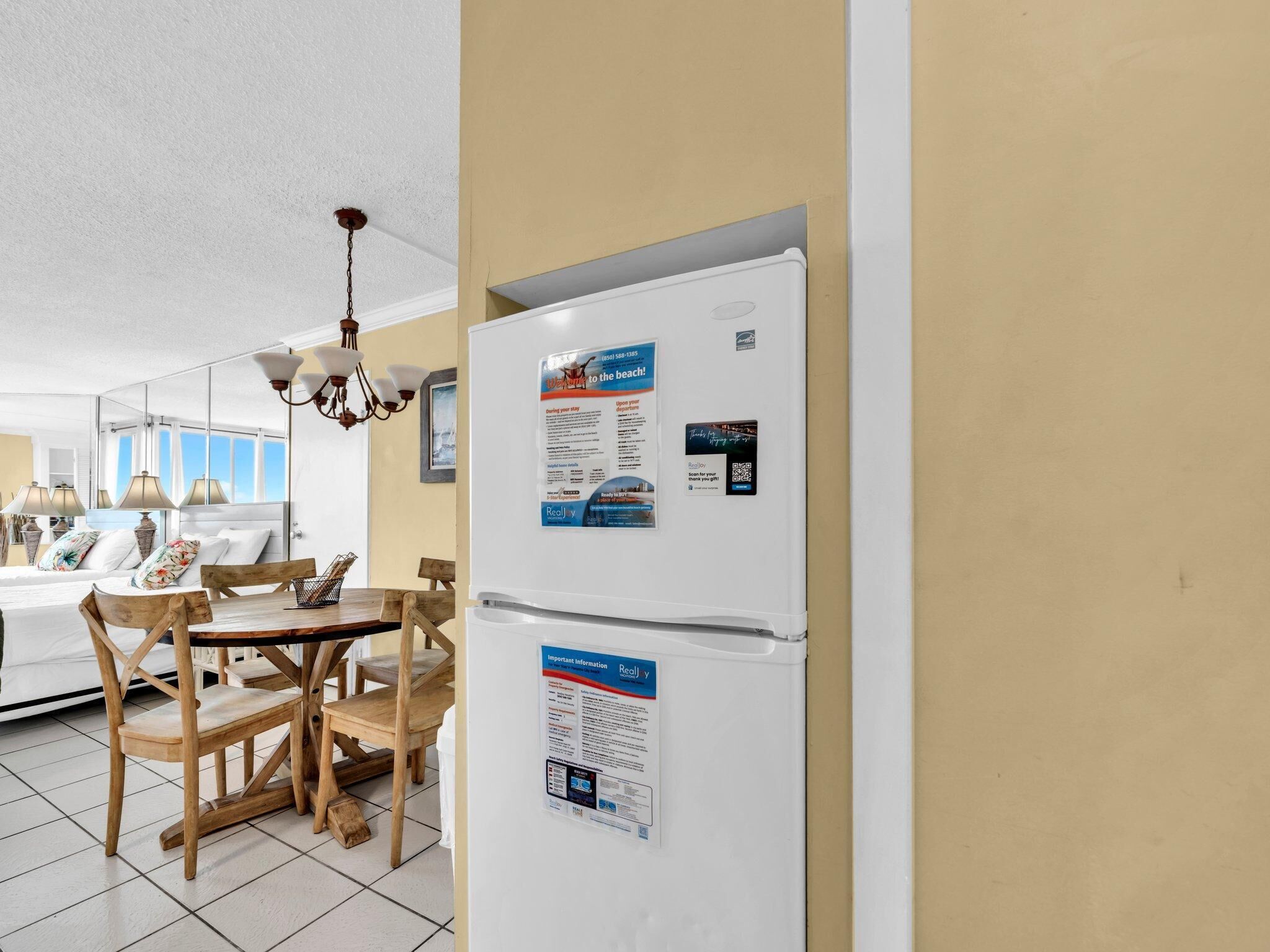 A kitchen with a white refrigerator, wooden dining table, and chairs. There is a chandelier above the table.