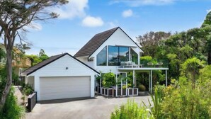 A modern two-story house with a large garage, a covered porch with plants, and a lush garden.