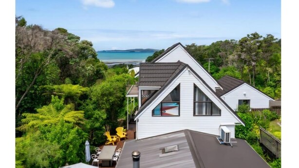 A white house with a gabled roof, a small deck, and a view of the ocean.