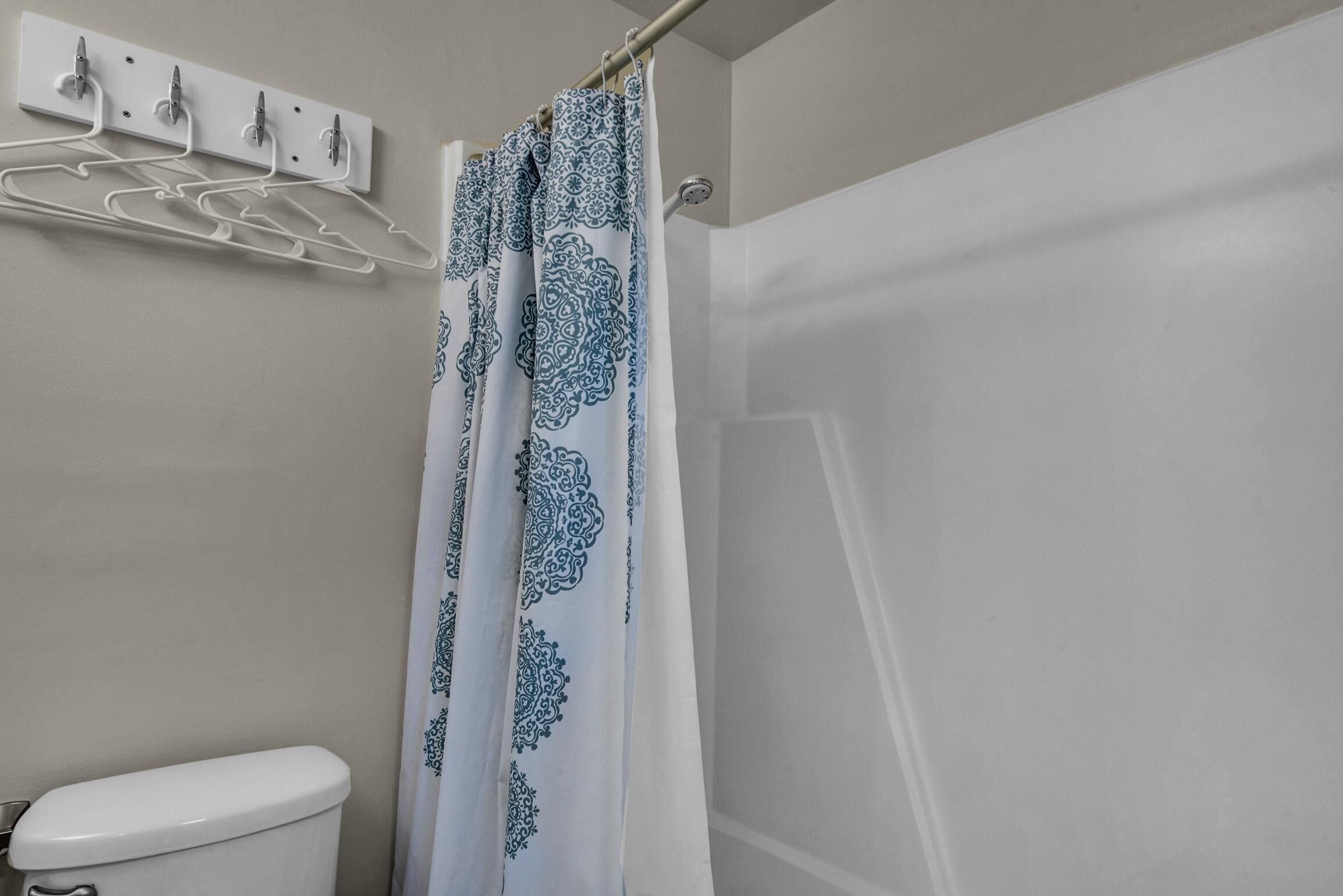 A bathroom with a toilet, a shower curtain with a blue pattern, and a wall-mounted towel rack with multiple hooks.