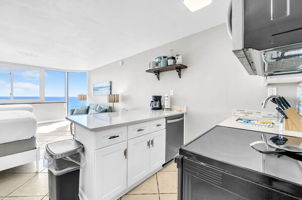 A modern kitchen with white cabinetry, a coffee maker, and a view of the ocean. - Top of the Gulf 813 (Panama City Beach)